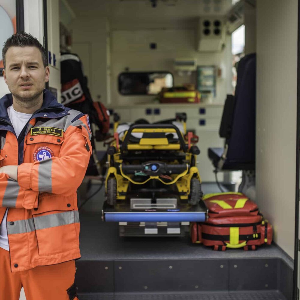 Portrait of a doctor or paramedic in uniform standing  in front of an ambulance vehicle, stretcher in background.